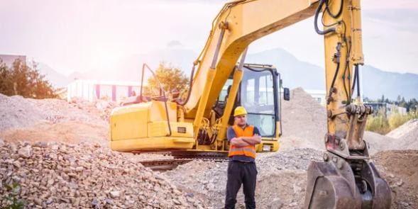 Construction worker standing in front of an excavator on a job site